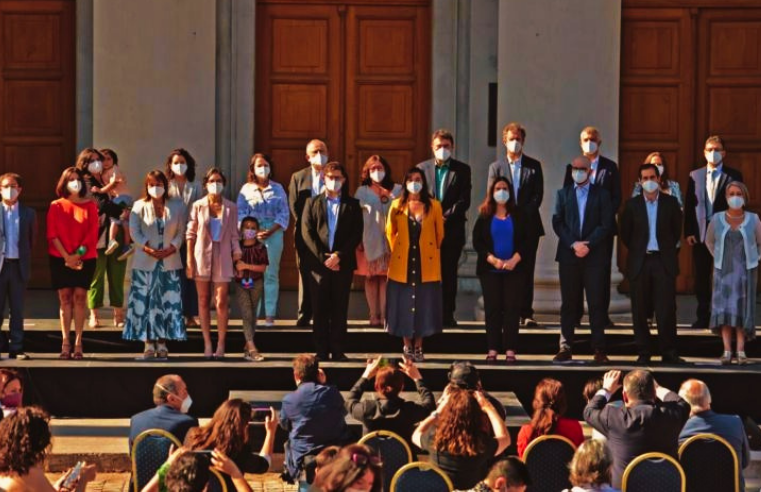 Borac, presidente do Chile, ao lado de 14 mulheres ministras e 10 ministros portando máscaras e postados na escadaria de um palácio, sendo fotografados por repórteres